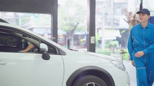 Asian automotive mechanic repairman giving a car service to client man. alt