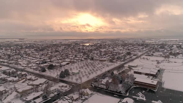 Aerial view flying over snow covered town towards the sunset alt