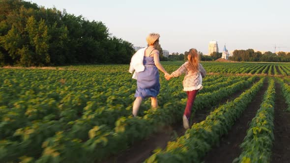 Mother and Daughter Run Across the Field at Sunset Holding Hands