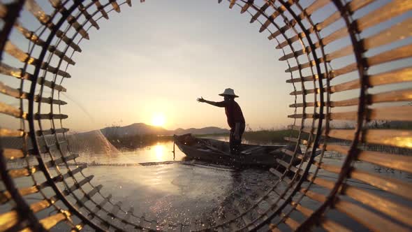 Silhouette fisherman throwing fishing net during sunset with boats at the lake.