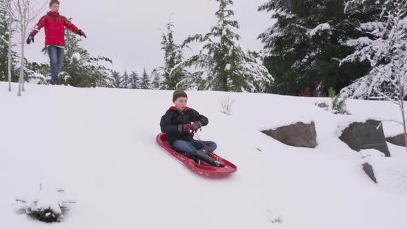 Young boy sledding down snow covered hill in winter