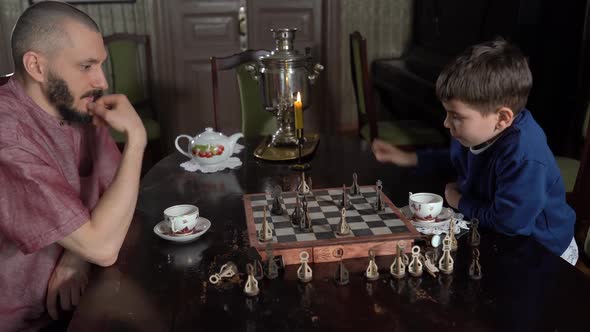 Side View Cute Little 6s Son and Young Father Play Chess Seated Indoor alt