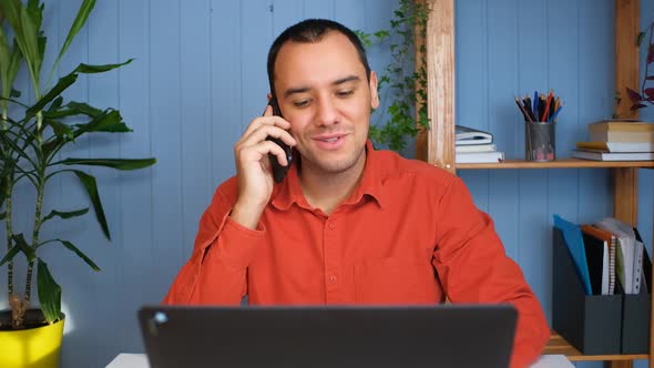 Smiling Young Business Man Professional Talking on Phone Using Laptop Sit at Home Office Desk