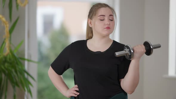 Middle Shot of Young Charming Plump Woman Exercising with Dumbbell at Home and Yawning alt