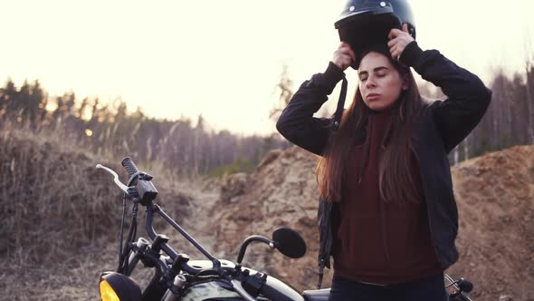 Beautiful Young Female Motorcyclist with a Black Motorcycle Helmet. Biker Girl Puts on Her Helmet on