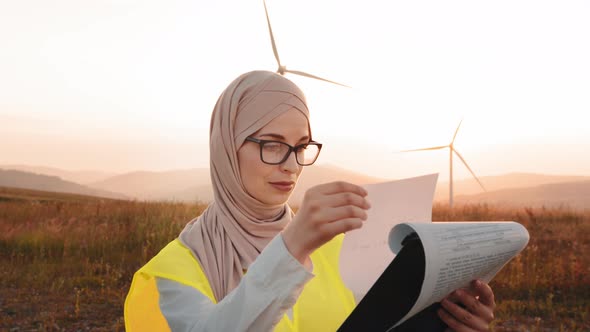 Charming Muslim Woman in Hijab and Eyeglases Holding Clipboard in Hands While alt