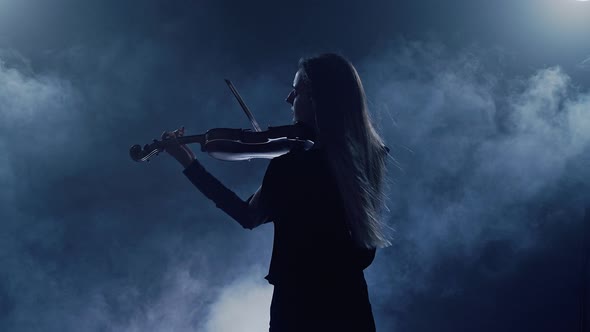Young Beautiful Woman Playing a Melody on Violin. Smoky Dark Studio
