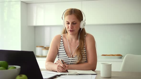 Woman Writing and Listening While Self Study at Table with Laptop in Home Room Spbd alt