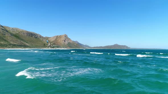 Wide Aerial Shot of Lone Kiteboarder Surfing Waves with a Mountainous Backdrop