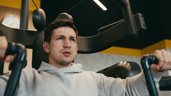 Young Man in Gray Hoodie Training Arms in a Gym