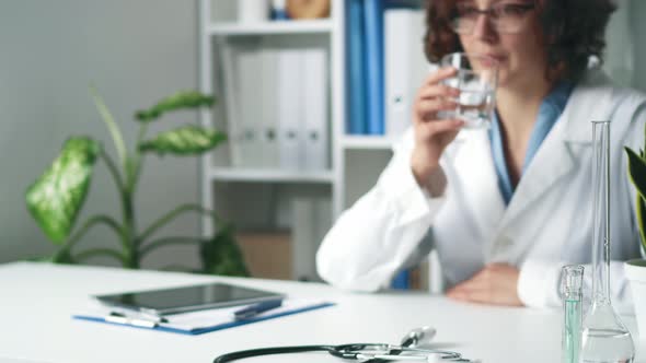 Girl Medical Doctor Sits At The Desk. The Doctor Drinks Water While Sitting In The Medical Office alt