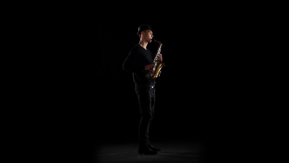Saxophonist Playing on the Instrument. Black Background in the Studio alt
