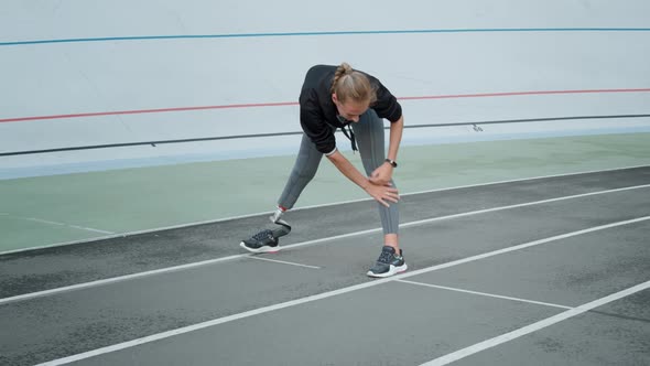 Runner with Prosthetic Leg Preparing for Workout on Track. Woman Stretching Body alt