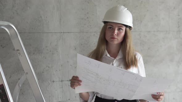 The girl engineer builder is checking the drawings at the apartment of the projected house. alt