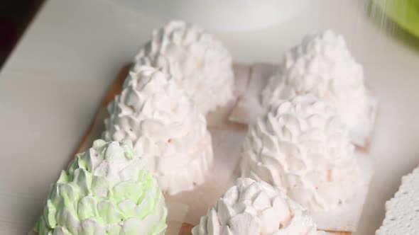 A Woman Sprinkles Powdered Sugar On Marshmallow Cones. Marshmallow Cones Of White And Light Gree alt