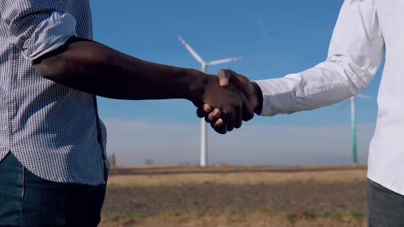 Two Male African American Electrical Engineers Stand Against the Backdrop of a Windmill at an Air alt