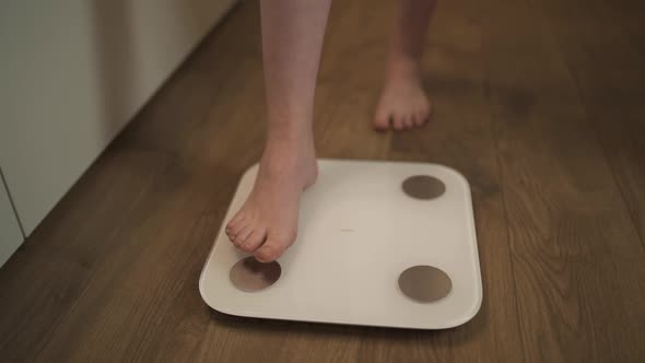 A Woman at Home Gets Her Feet on the Scales To Measure Her Weight alt