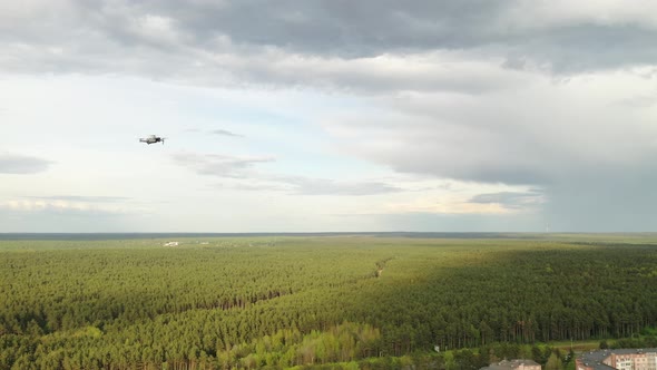 A Hovering Drone Flies Up Against the Background of a Cloudy Sky and Forest alt