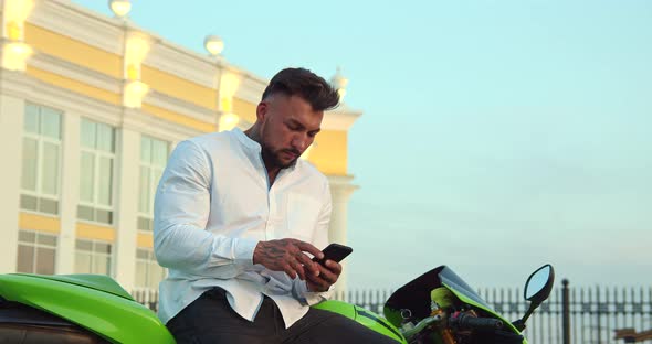 Man Sitting on Motorcycle and Using Smartphone in City