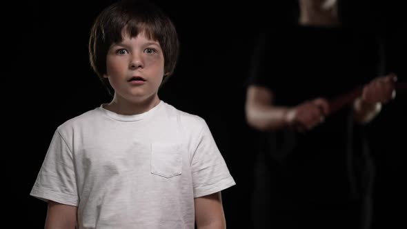 Frightened Caucasian Boy with Scared Facial Expression Looking at Camera As Unrecognizable Mother alt