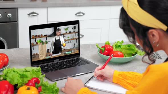 Woman in Kitchen Watch Online Cooking Course Listen Chef Writes in Notebook alt