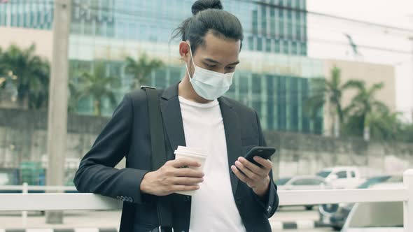 Portrait of a young businessman wearing a mask and using a smartphone.