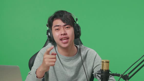 Asian Man Gamer With Headphone Waving Hand While Playing Game On Mobile Phone On Green Screen alt