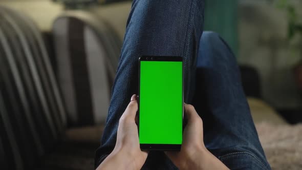 girl is resting at home on couch and holding smartphone with green screen. alt
