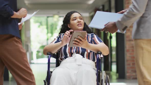 Smiling diverse business people with colleague in wheelchair talking in modern office alt