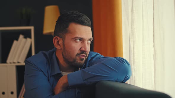 A Young Bearded Man Looks Out the Window and is Bored alt