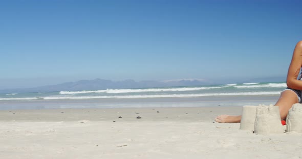 Mother and daughter making sand castle at beach alt