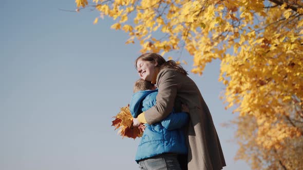 Happy Family Plays with Bouquet of Yellow Leaves in Autumn Park alt
