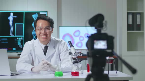 Asian Scientist Researching In The Laboratory With A Microscope, He Warmly Smiles Into The Camera alt