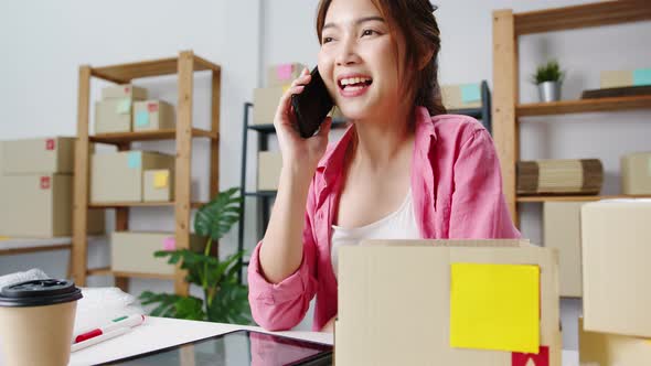 Young Asian woman using phone call receiving purchase order and check product on stock work at home. alt
