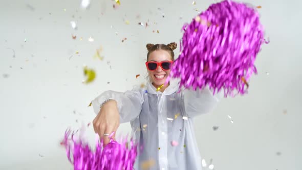 A Smiling Girl with Red Glasses Shakes Pompoms Under Falling Confetti