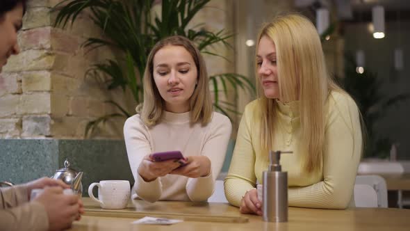 Charming Young Woman Scanning QR Code on Table in Restaurant with Phone App Sitting with Friends alt