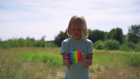 Blonde Boy in the Park Plays Popit Rainbow Colors