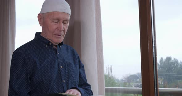 An Old Muslim Man Reading Koran at Home