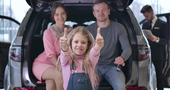Portrait of Pretty Caucasian Little Blond Girl Showing Thumbs Up As Her Happy Parents Sitting at the alt