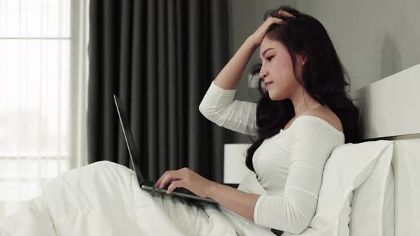 stressed woman using a laptop computer on bed