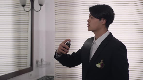 Side View of Young Asian Man in Wedding Suit Spraying Perfume in Slow Motion Smelling Fragrance alt