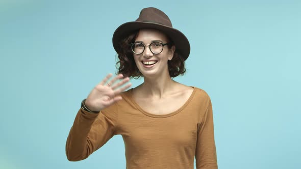 Beautiful Girl Traveler in Hipster Hat and Glasses Saying Hi Smiling Friendly and Waving Hand in