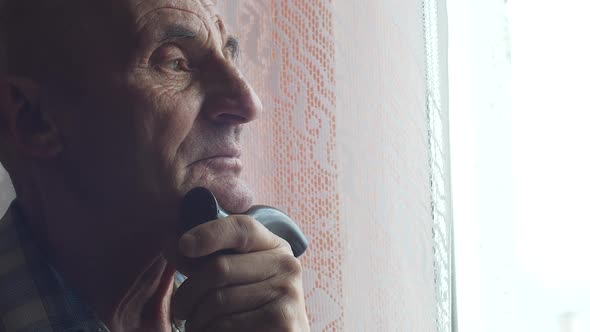 Portrait of a pensive caucasian pensioner 70 years old with a walking stick bored at the window.The  alt