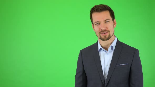 A Young Businessman Talks To the Camera with a Smile, Gestures Toward It and Next To Himself alt