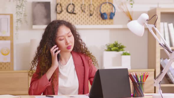 Business woman professional talking on phone using tablet sitting at home office desk, serious talk alt