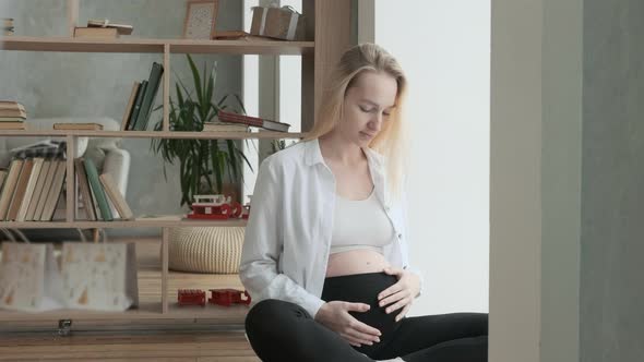 pregnant european woman at the window touches her tummy