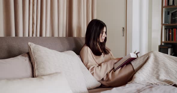 Woman Reading a Book Lying on Bed at Home alt