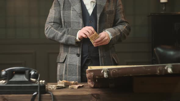 Mafia Gangster in Plaid Suit in  Stands at Table in Room and Counts Old Money alt