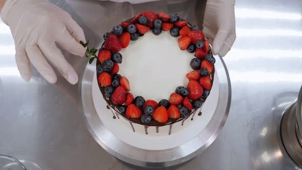 A Pastry Chef Decorates a Cake with Berries and Mint Leaves in a Pastry Shop alt