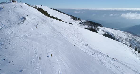 Forward Aerial Top View Over Winter Snowy Mountain Ski Track Field with People in Sunny Day